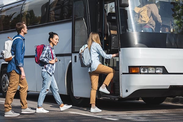 side view of multicultural friends with backpacks walking into travel bus at street