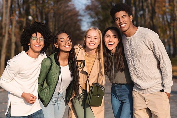 Cheerful multiethnic teenagers guys and girls embracing and posing at camera at park